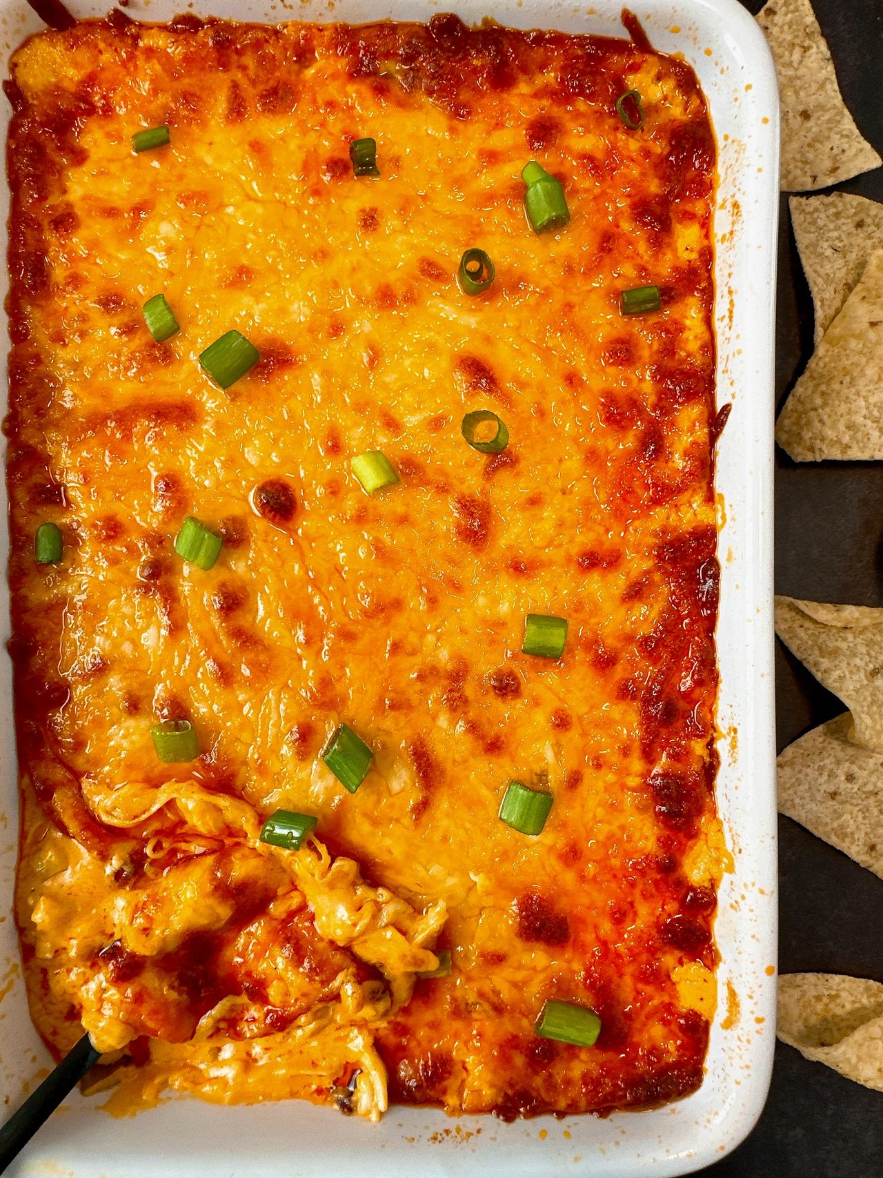Buffalo Chicken Dip in a white dish with corn chips on a black surface