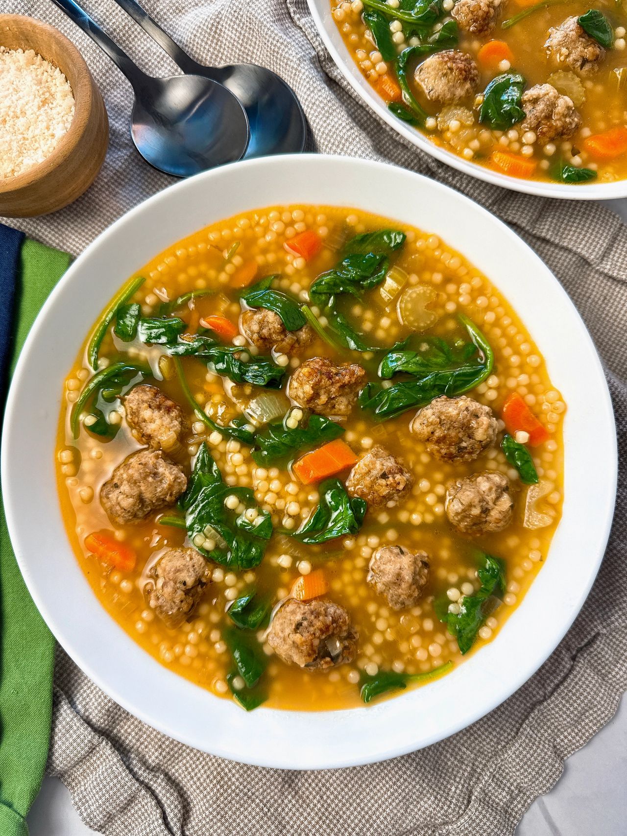 Italian wedding soup in a white bowl with a black spoon