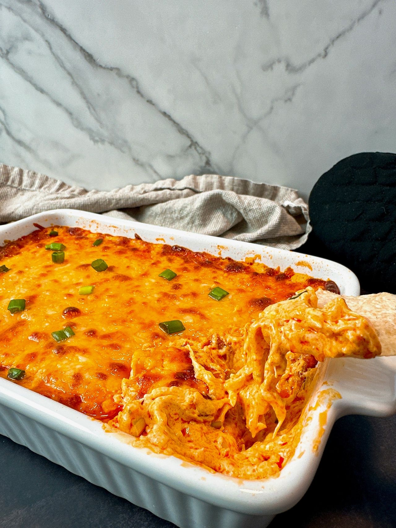 Buffalo Chicken Dip in a white dish with corn chips on a black surface