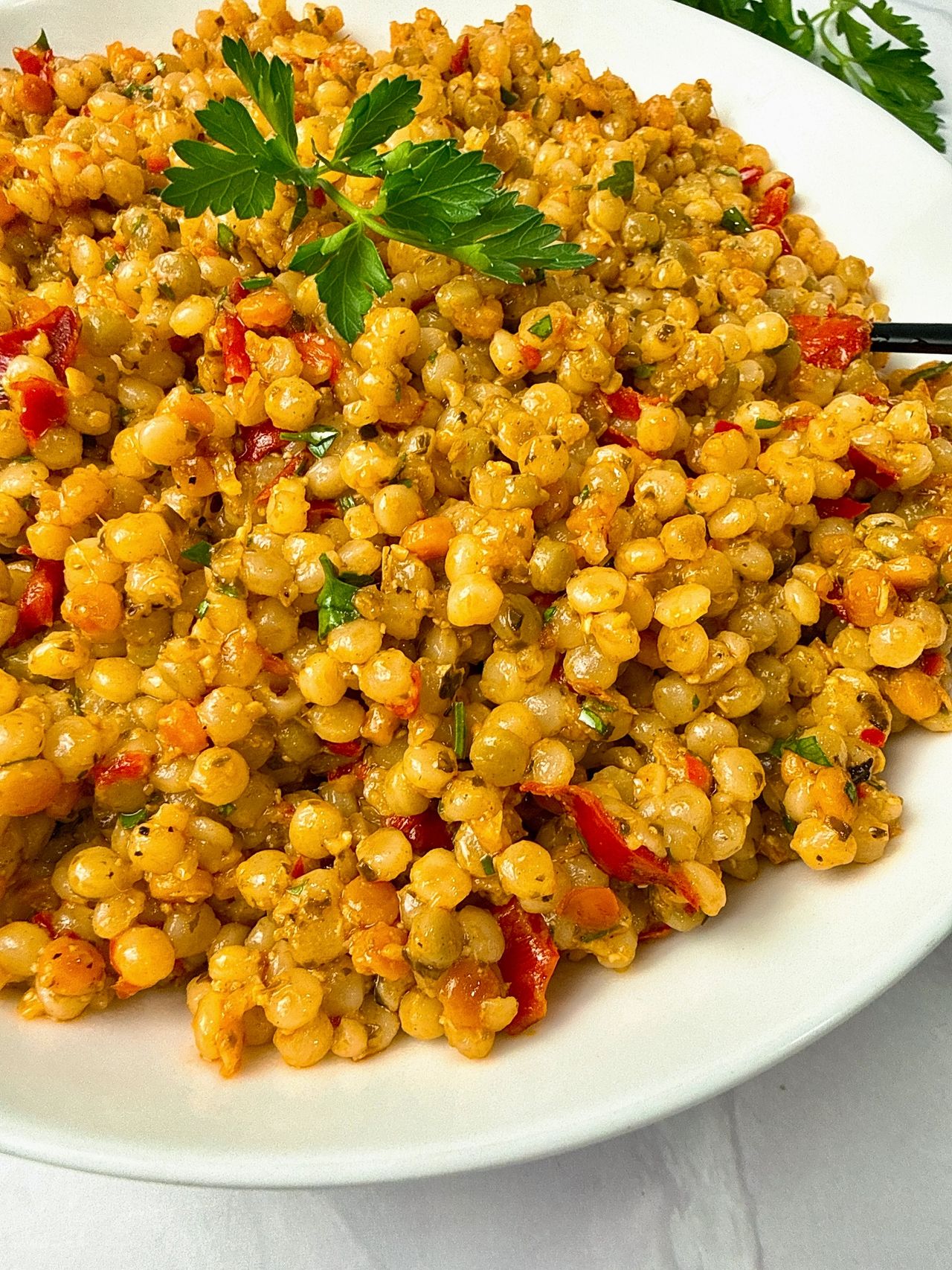 Couscous with Pesto and Peppers in a white bowl with a black spoon and fresh parsley