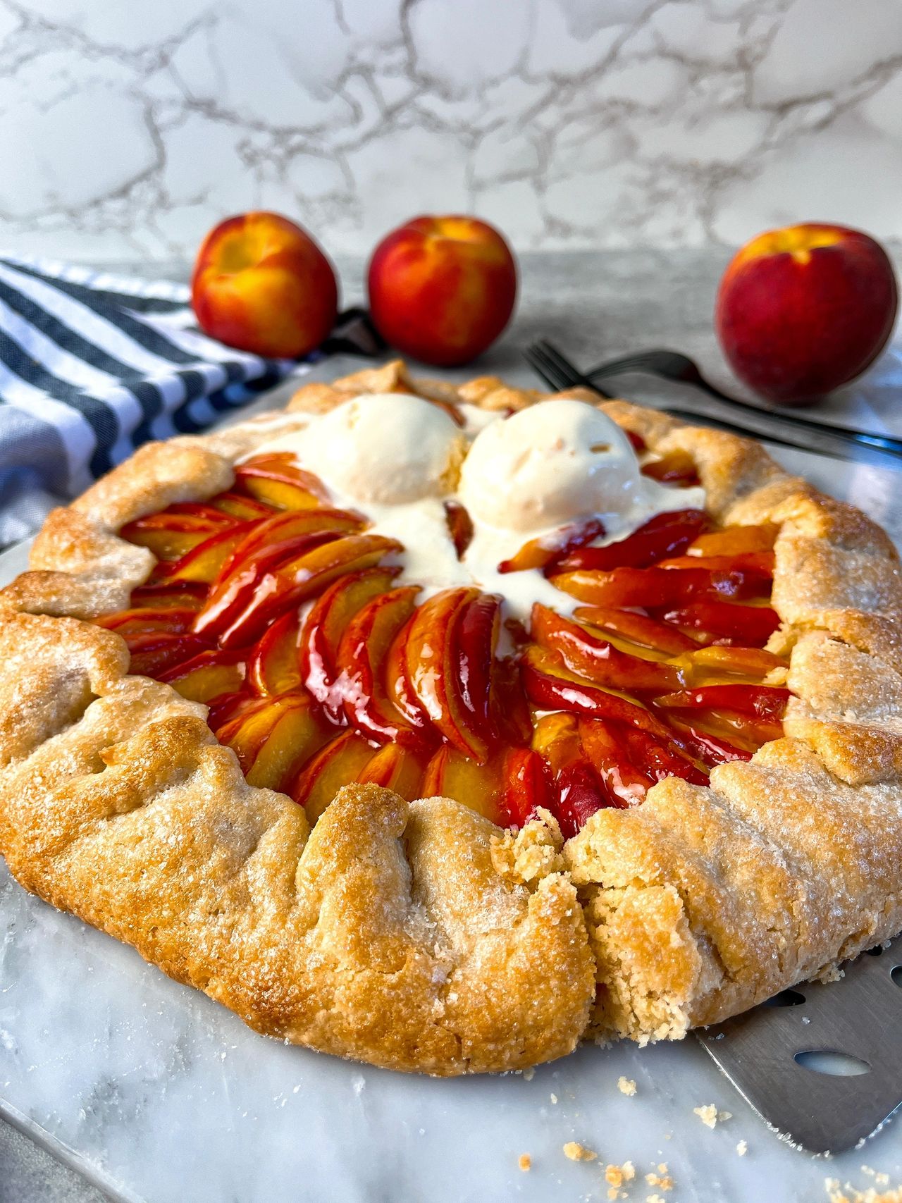 Easy Peach Galette on a marble surface with vanilla ice cream and peaches in the background