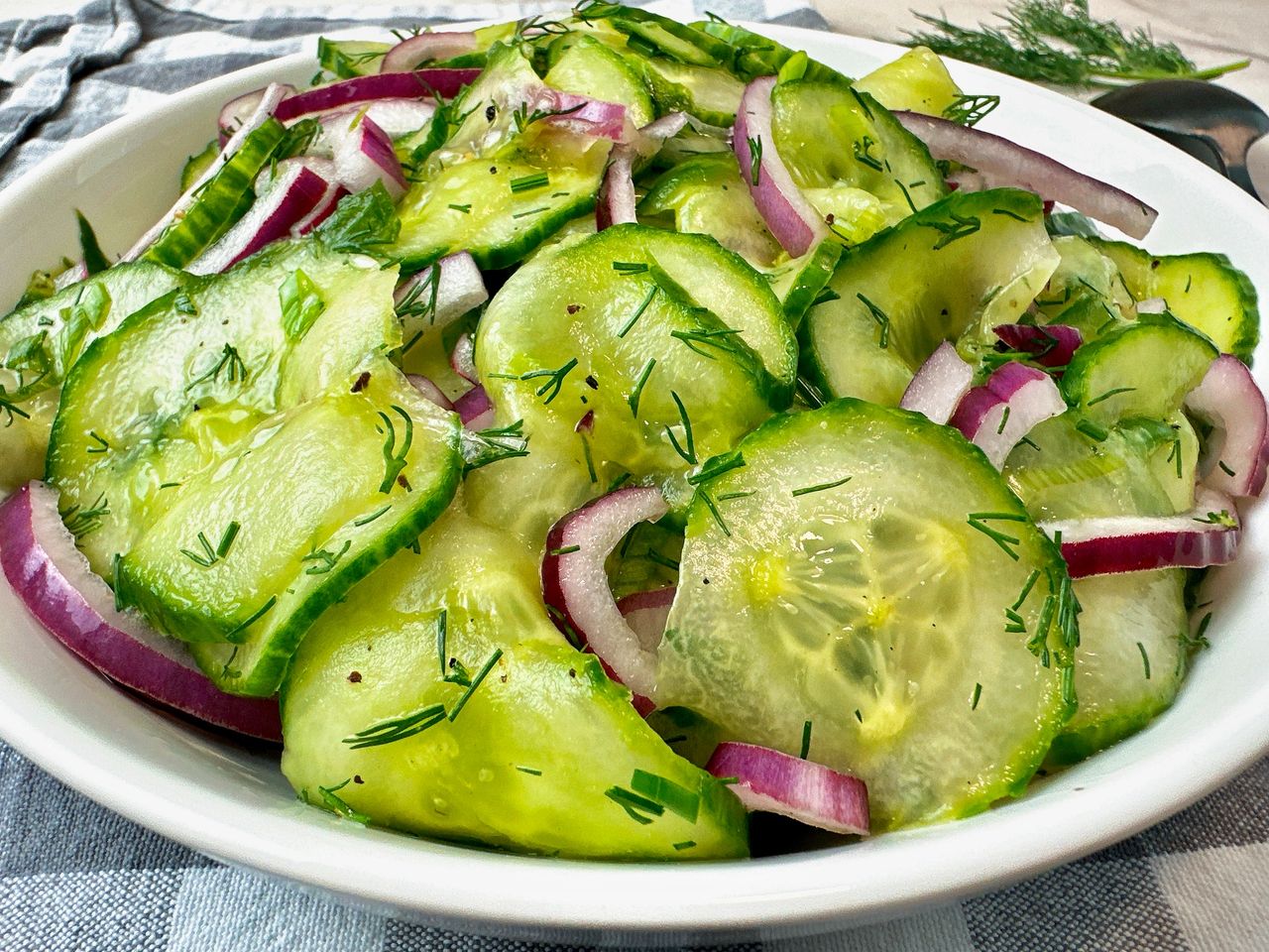 cucumber salad in a white bowl with a black spoon