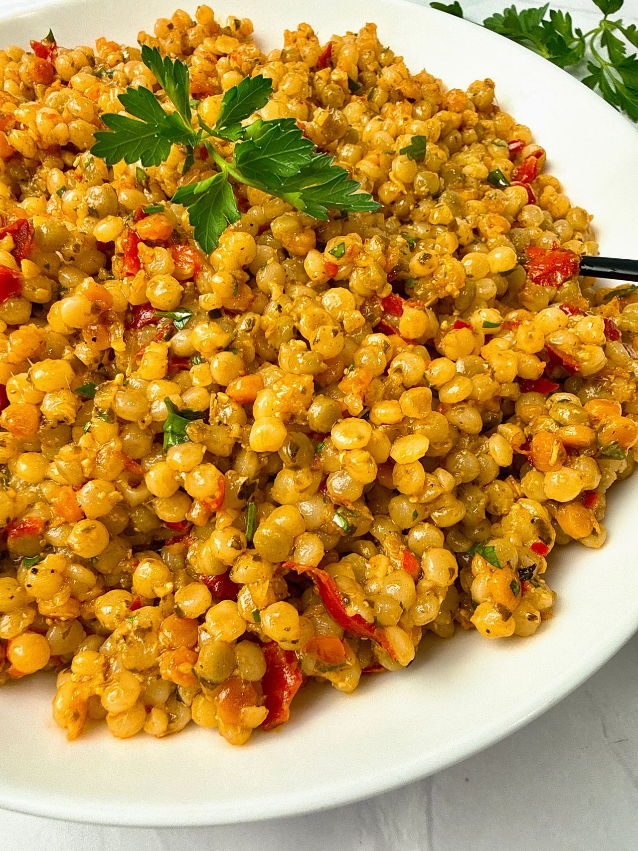 Couscous with Pesto and Peppers in a white bowl with a black spoon and fresh parsley