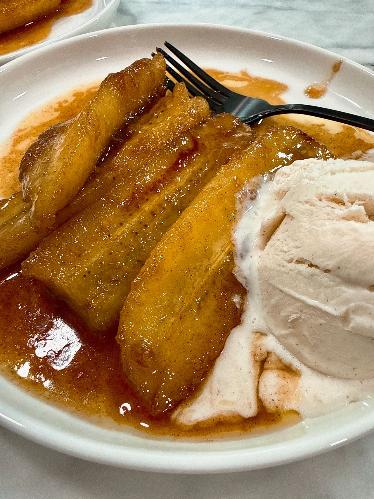 Bananas foster on a white plate with black spoon and vanilla ice cream