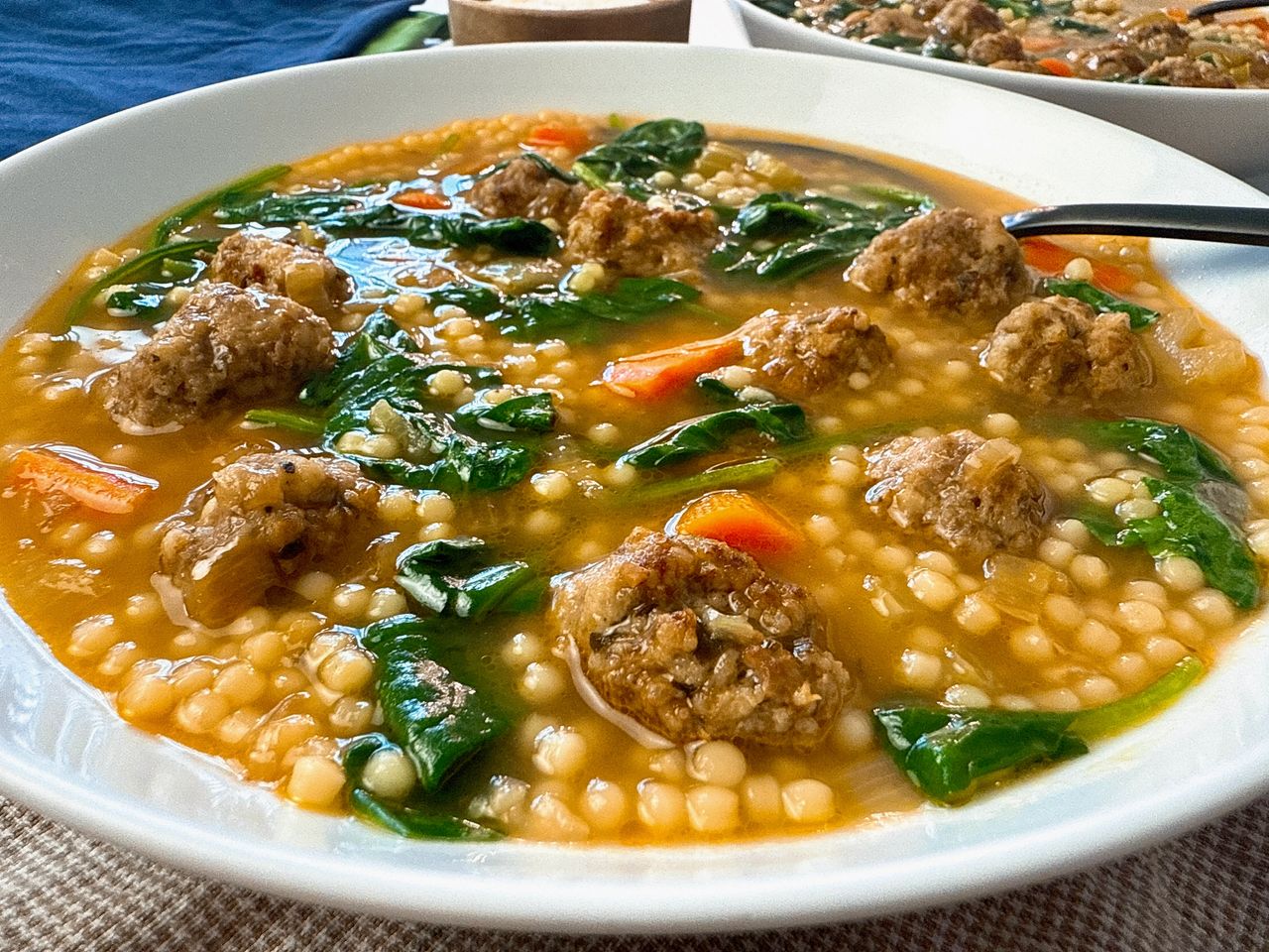 Italian wedding soup in a white bowl with a black spoon