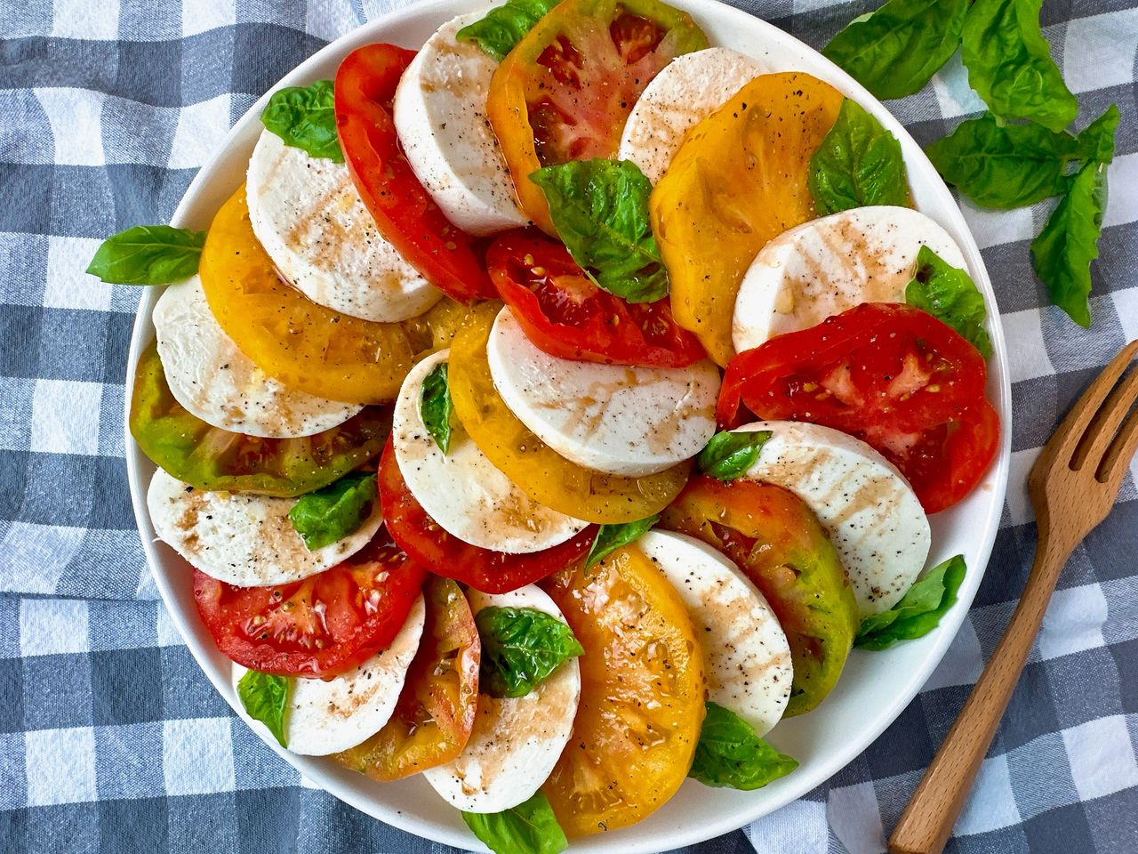Caprese Salad in a white bowl on a checkered towel with fresh basil leaves