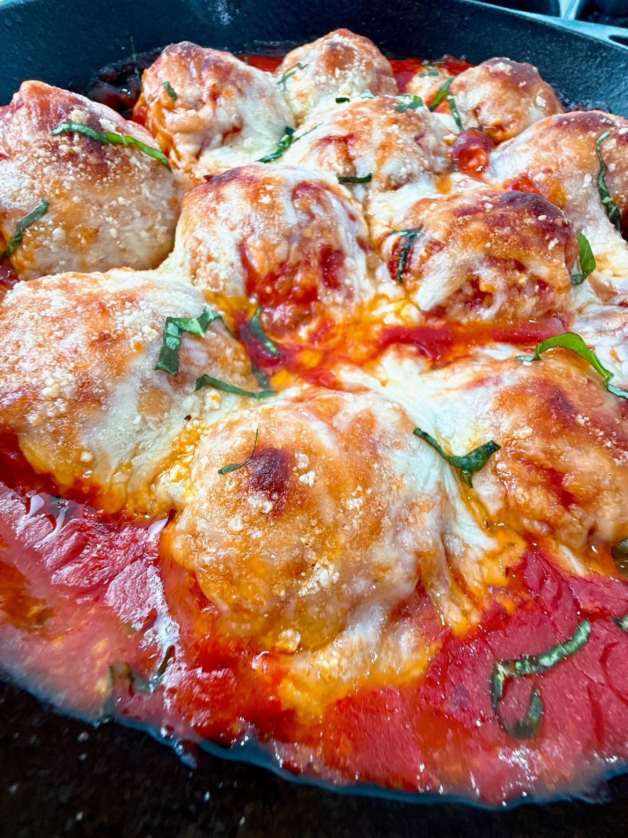 Chicken Parmesan Meatballs in a cast iron skillet with a black spoon and fresh basil