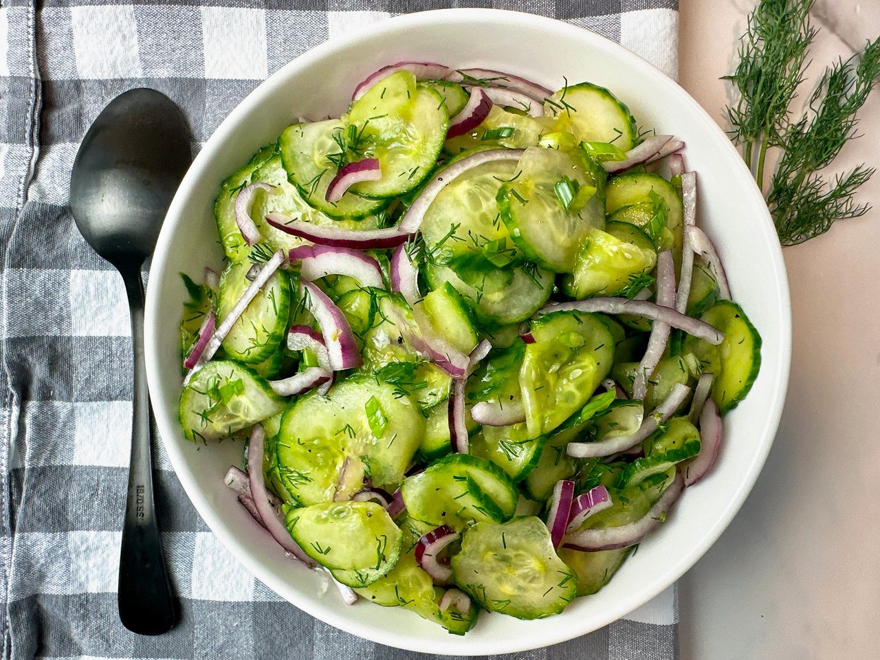 cucumber salad in a white bowl with a black spoon