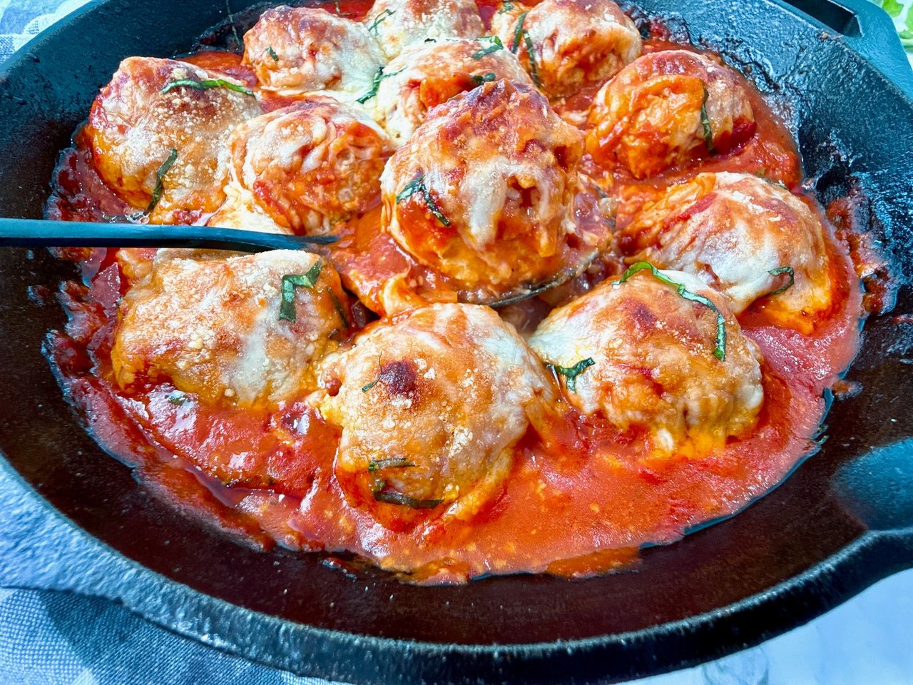 Chicken Parmesan Meatballs in a cast iron skillet with a black spoon and fresh basil