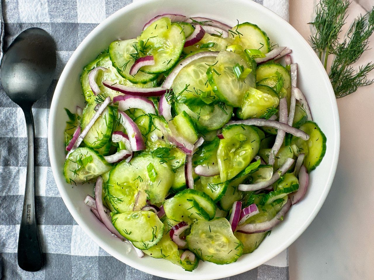 cucumber salad in a white bowl with a black spoon