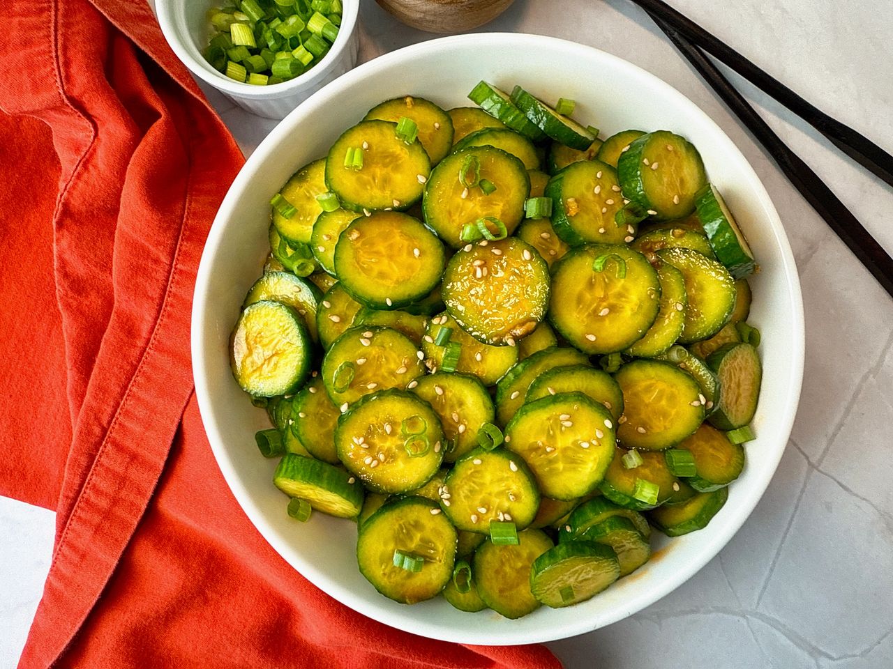 Asian Cucumber Salad in a white bowl with black chop sticks and red napkin