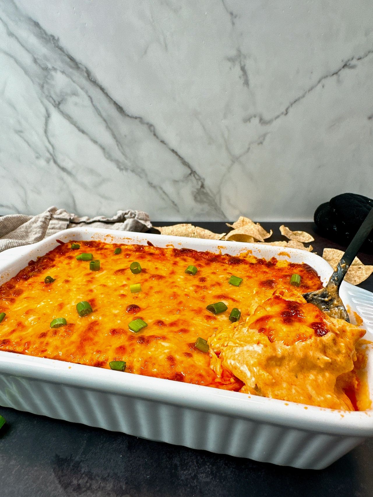 Buffalo Chicken Dip in a white dish with corn chips on a black surface
