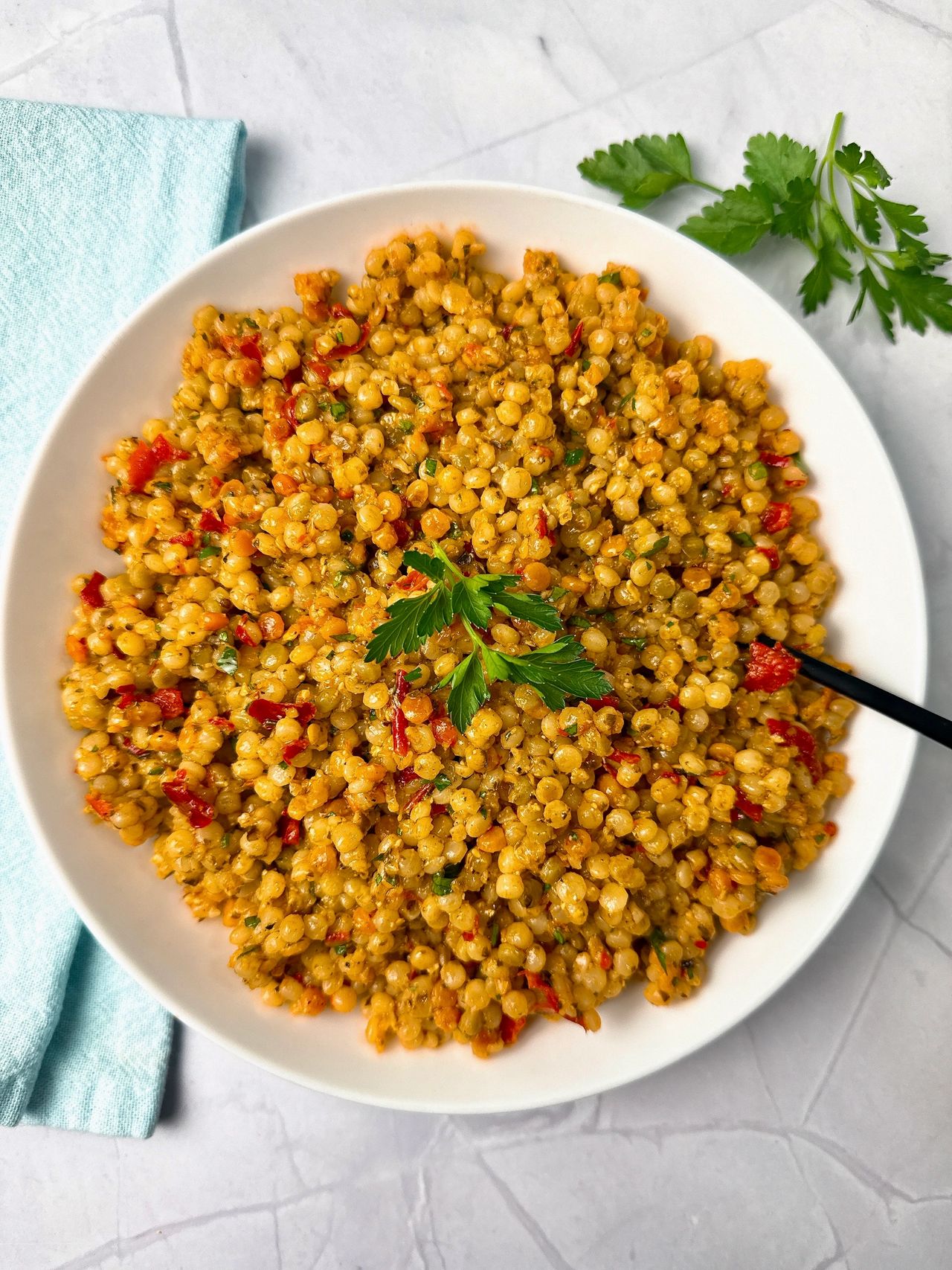 Couscous with Pesto and Peppers in a white bowl with a black spoon and fresh parsley