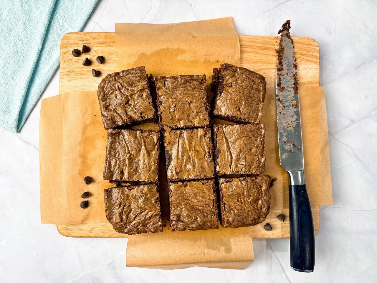 Ultimate Brownies on brown parchment paper with a knife and blue towel