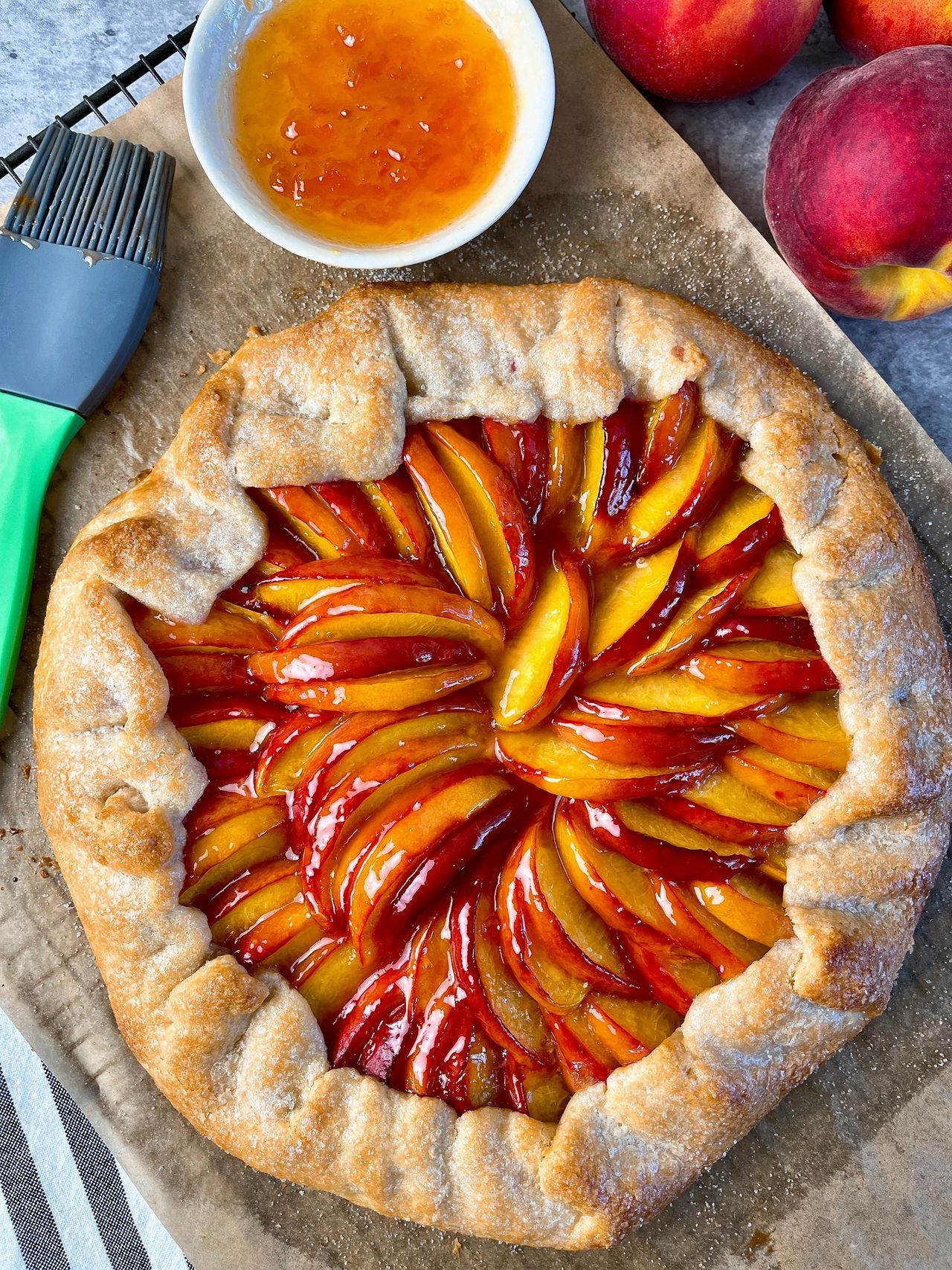 Easy Peach Galette on parchment paper with a bowl of preserves and pastry brush and peaches