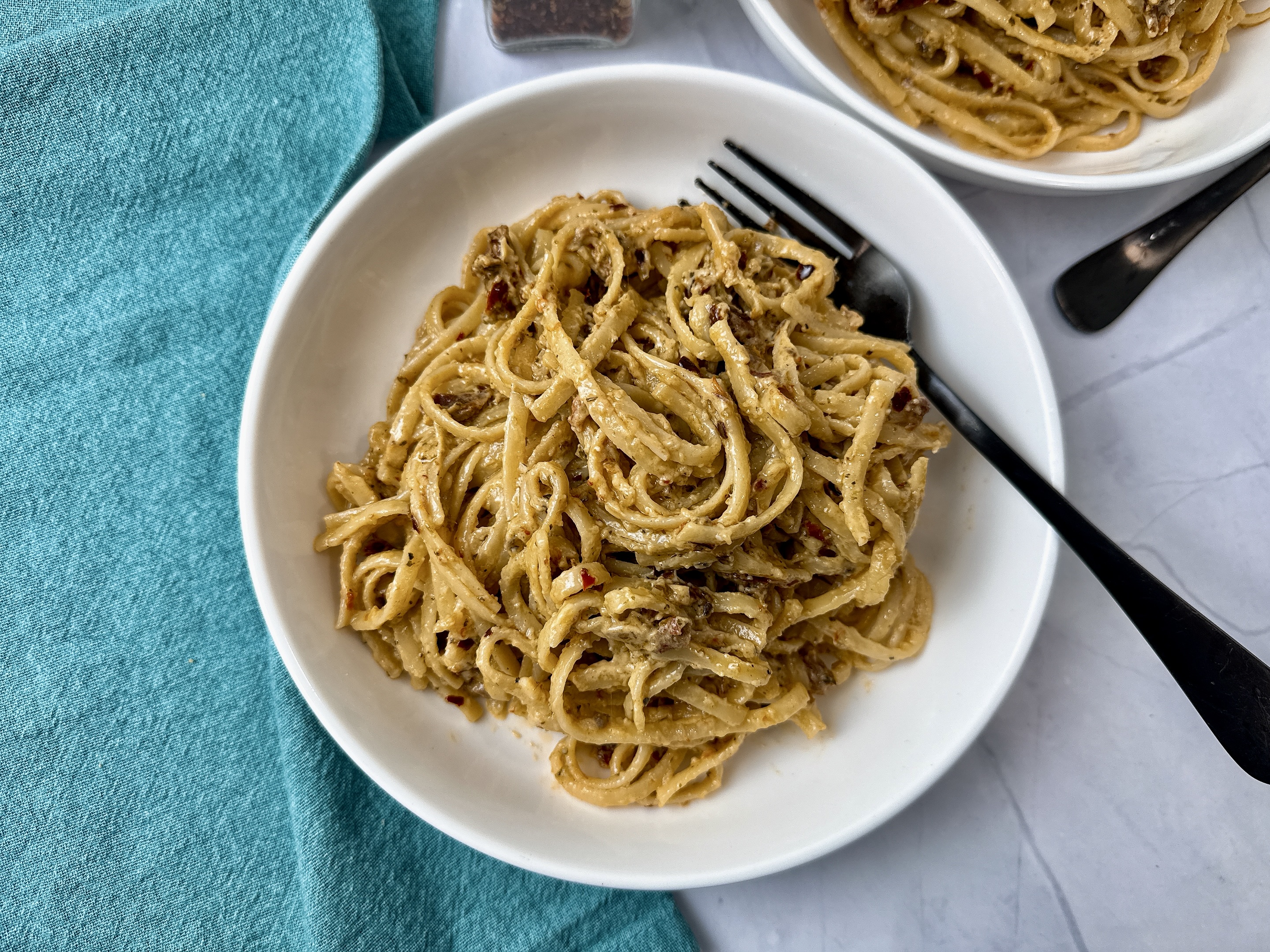 pasta with pesto and sun dried tomatoes in a white bowl