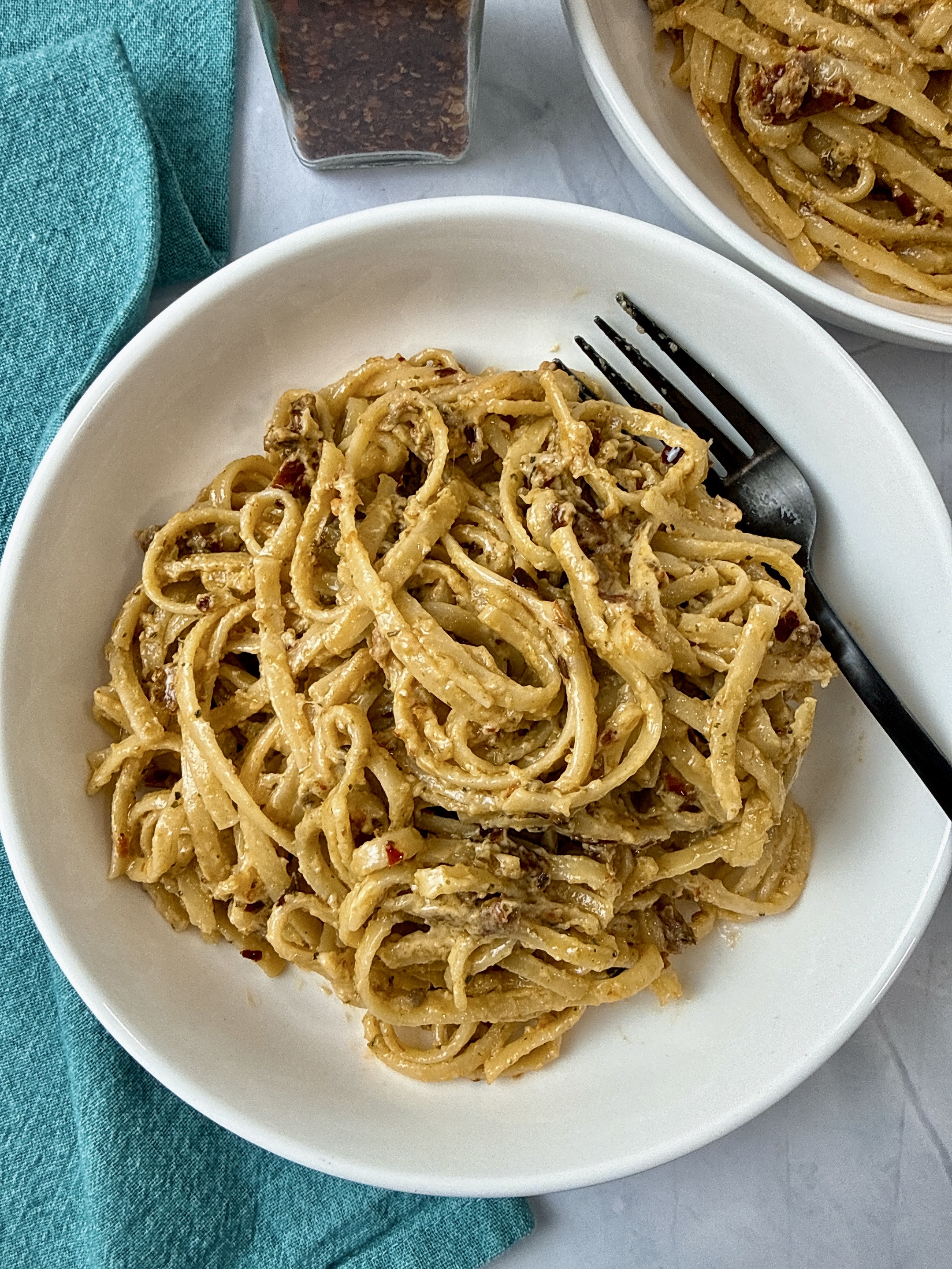pasta with pesto and sun dried tomatoes in a white bowl