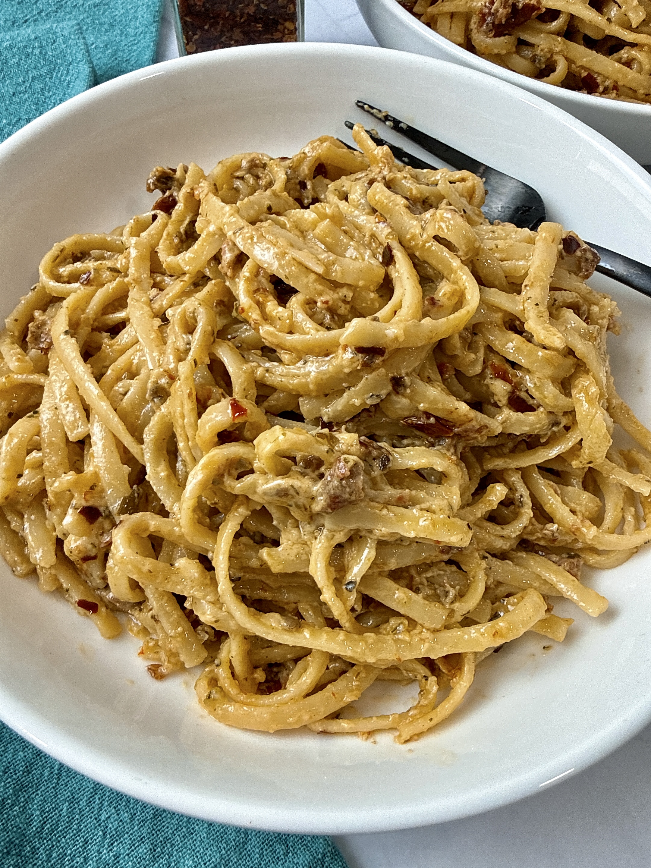 pasta with pesto and sun dried tomatoes in a white bowl