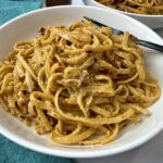 pasta with pesto and sun dried tomatoes in a white bowl