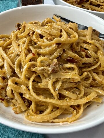 pasta with pesto and sun dried tomatoes in a white bowl