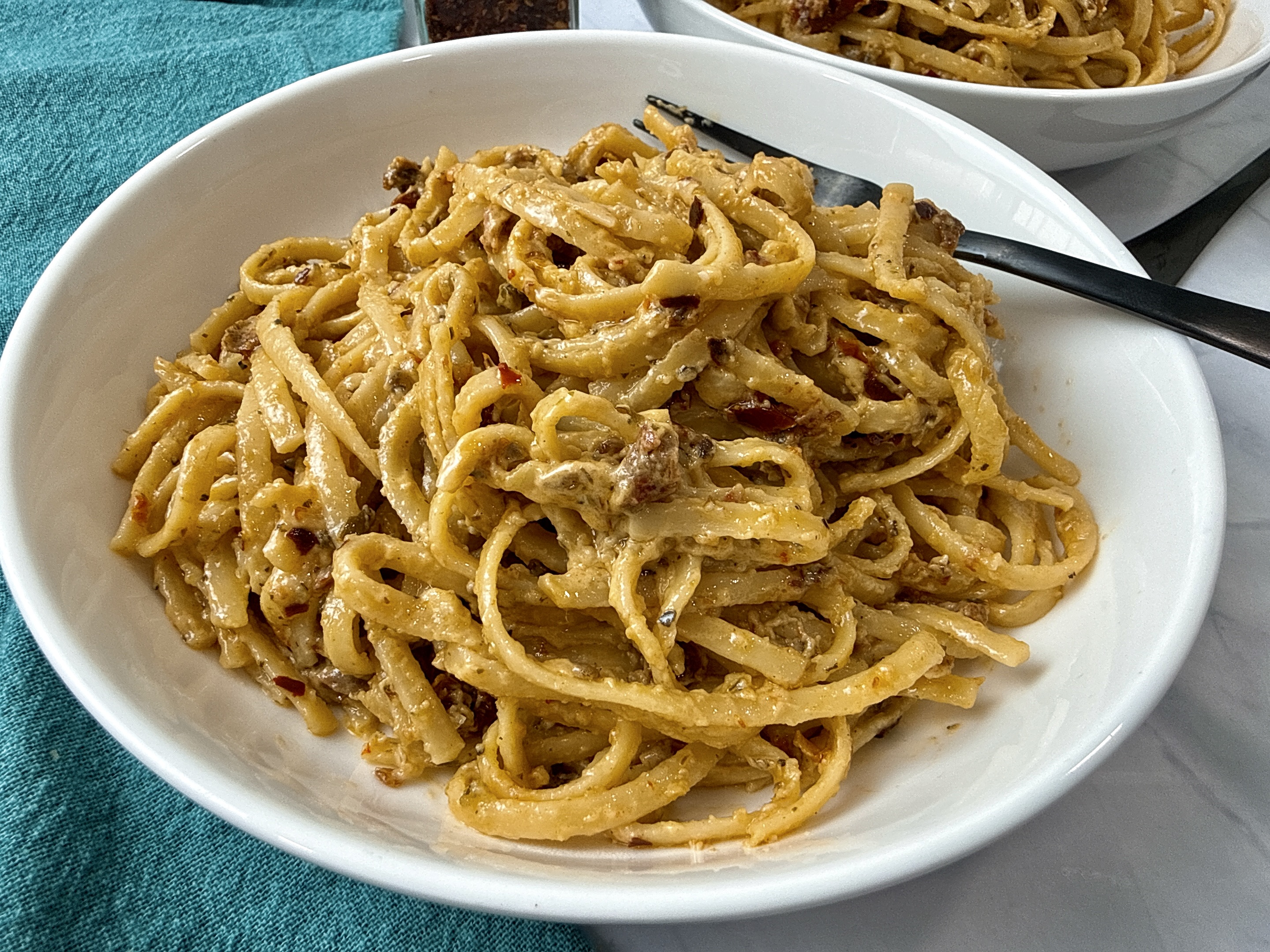 pasta with pesto and sun dried tomatoes in a white bowl