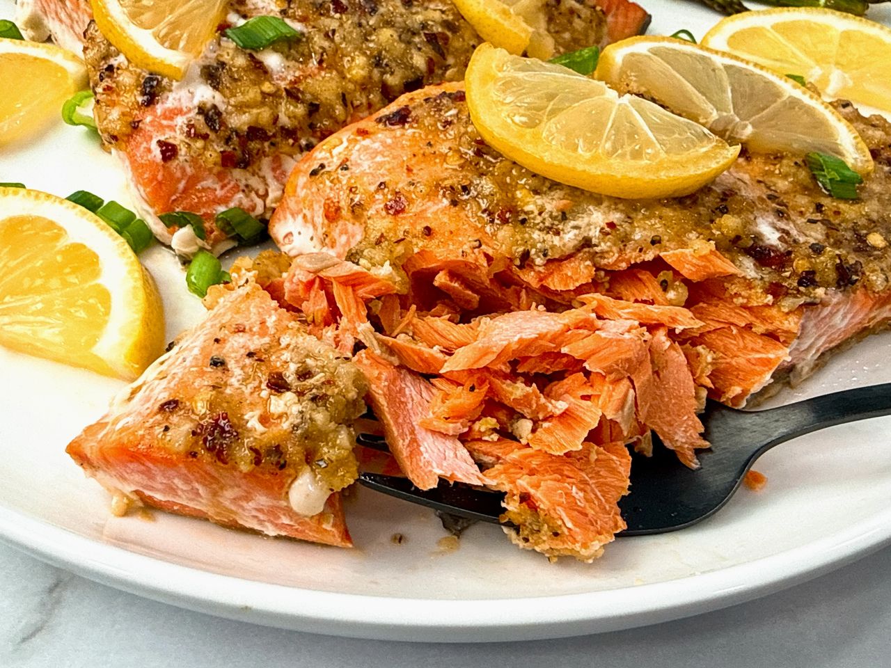 salmon on a white plate with lemon slices and a black fork