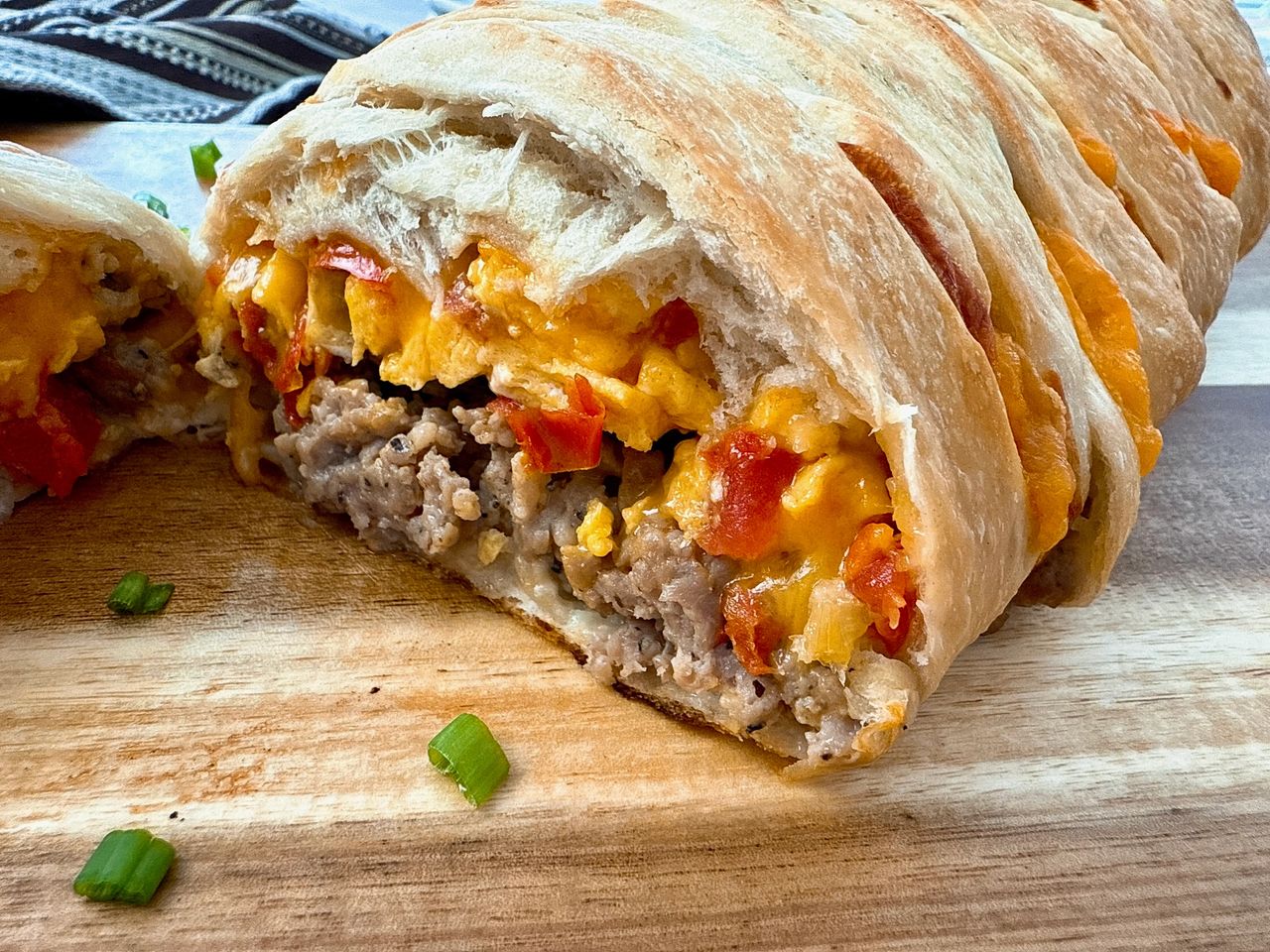 breakfast braid with eggs, cheese and sausage on a wooden cutting board
