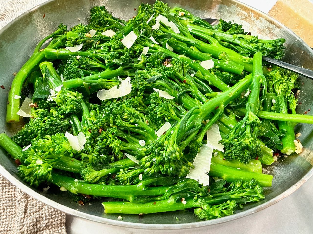 broccolini and pecorino romano in a silver skillet with black spoon and brown towel