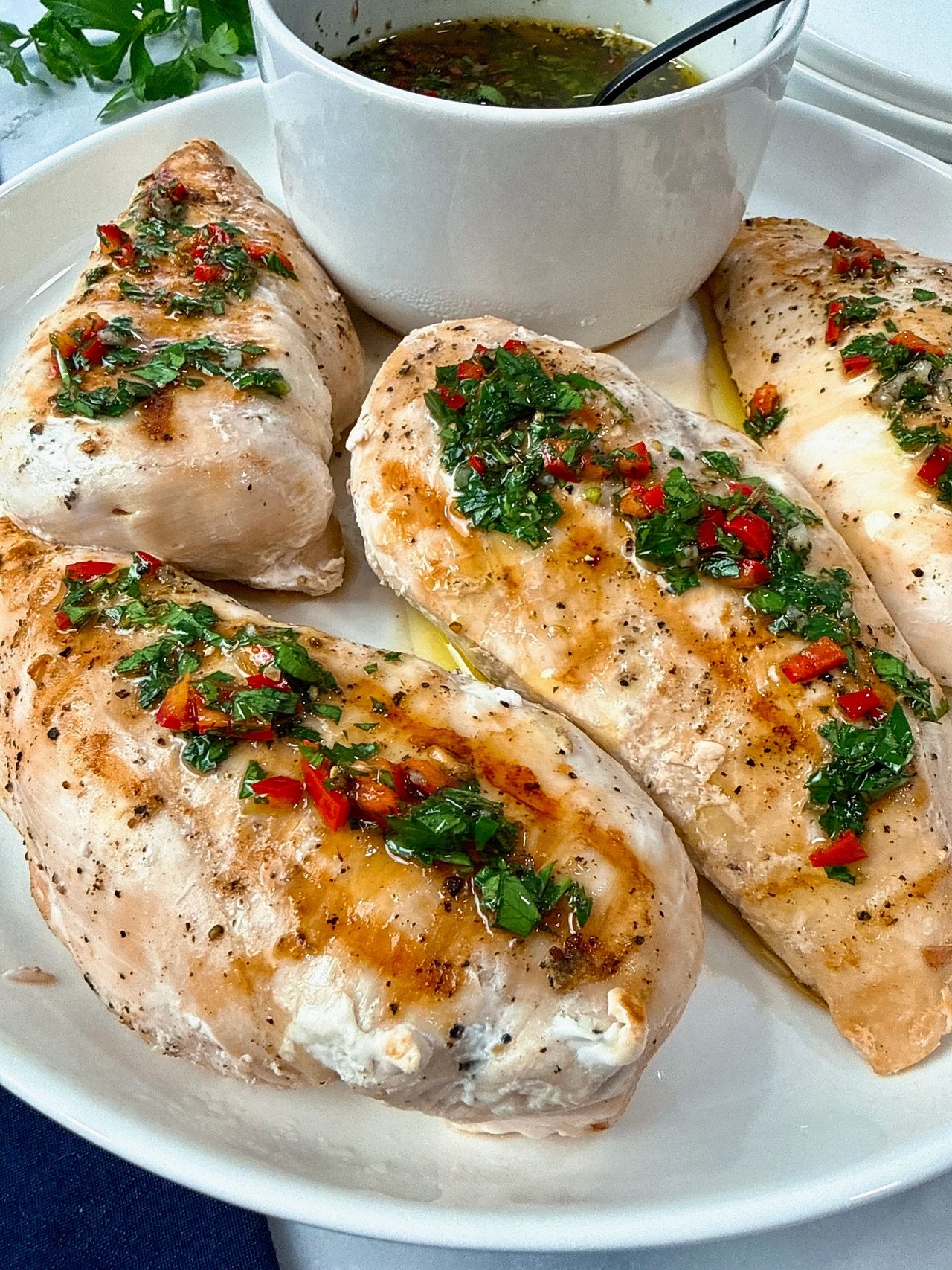 grilled chicken and bowl of chimichurri sauce on a white plate with a black spoon