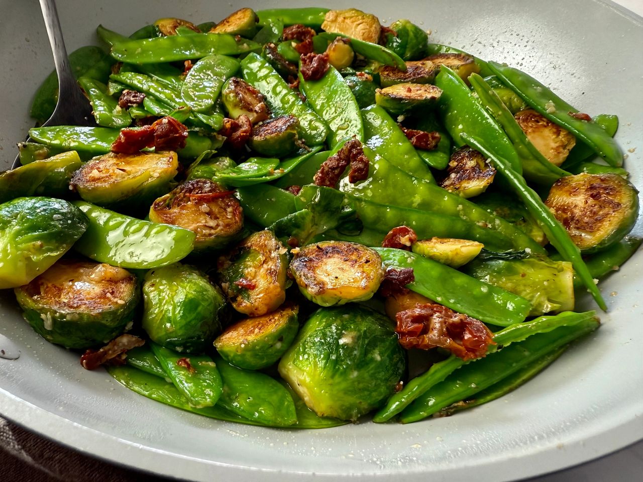 brussels sprouts, snow peas, and sun dried tomatoes in a white skillet