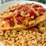 chicken breast with roasted red peppers over rice on a white plate