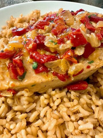 chicken breast with roasted red peppers over rice on a white plate