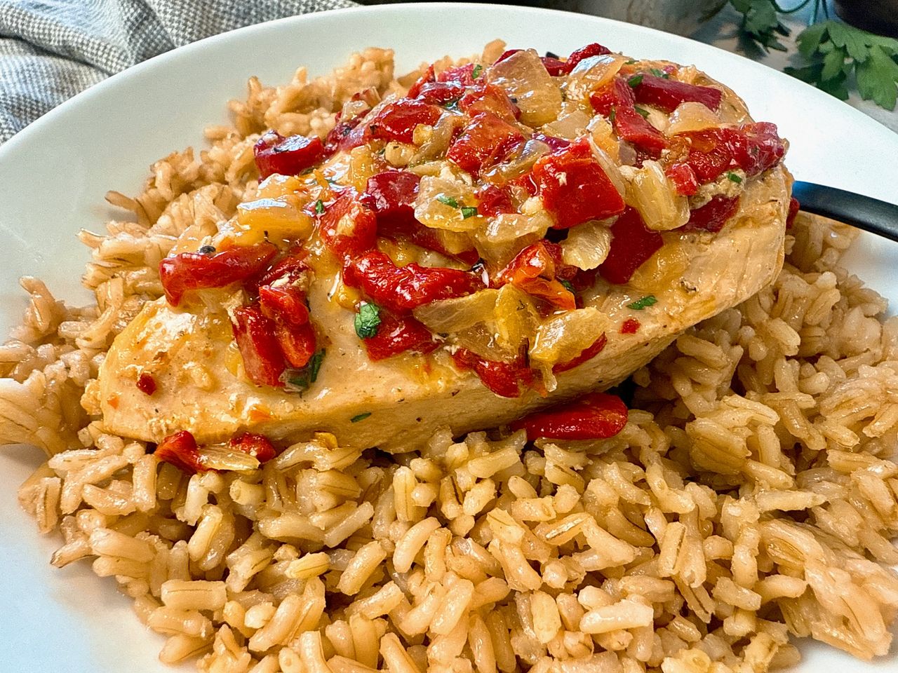 chicken breast with roasted red peppers over rice on a white plate