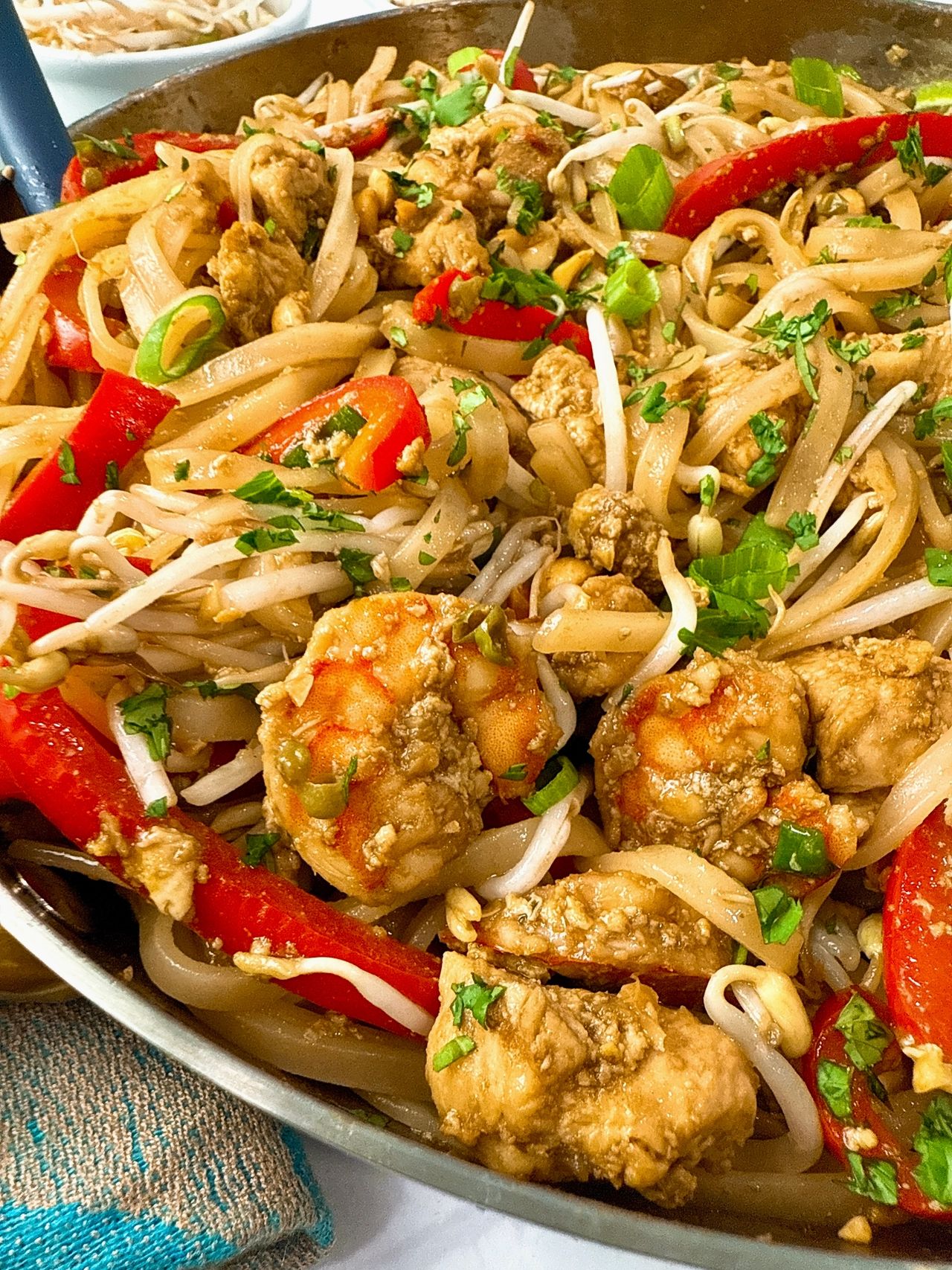 pad thai in a silver skillet with peanuts on the side