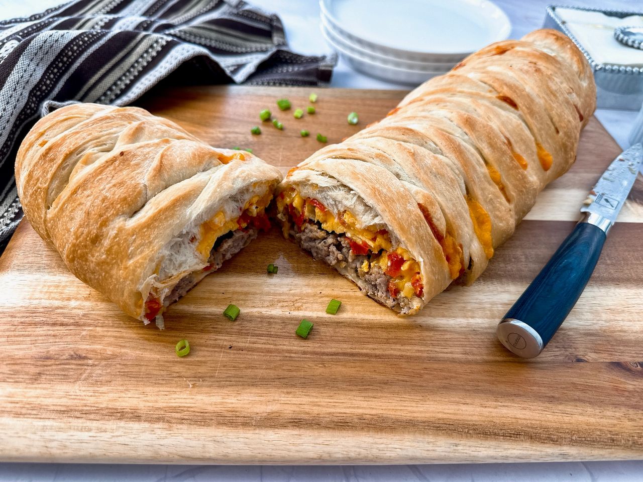 breakfast braid with eggs, cheese and sausage on a wooden cutting board