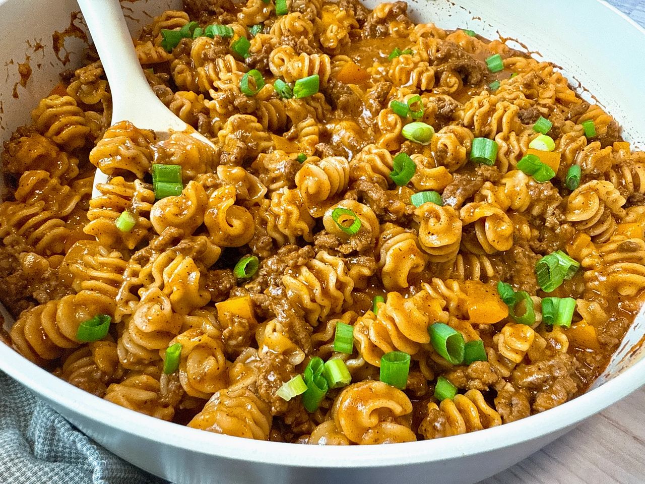 beef and pasta in an enchilada sauce in a white pan with a white spoon