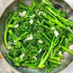 broccolini and pecorino romano in a silver skillet with black spoon and brown towel