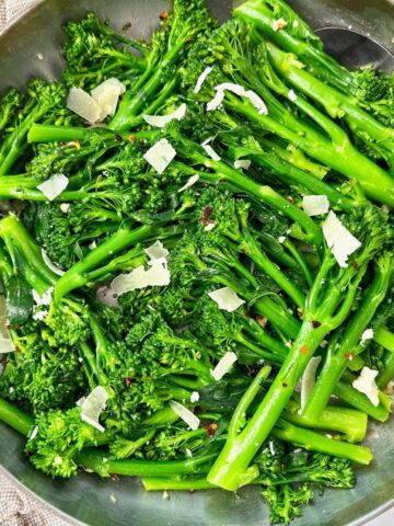 broccolini and pecorino romano in a silver skillet with black spoon and brown towel