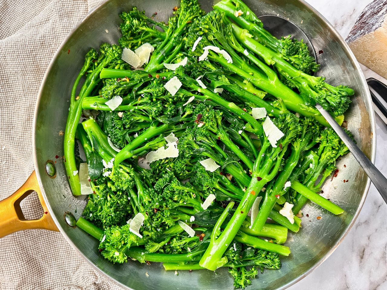 broccolini and pecorino romano in a silver skillet with black spoon and brown towel