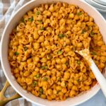 pasta and peas in a white saucepan with a white spoon