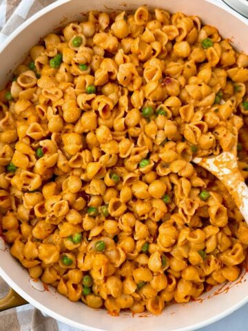 pasta and peas in a white saucepan with a white spoon