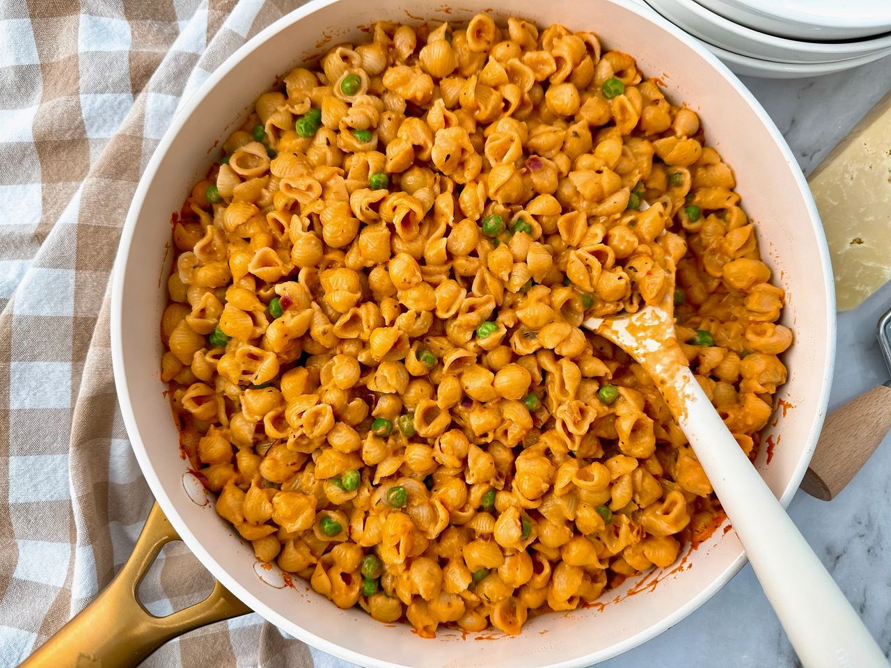 Creamy Pasta and Peas in a white saucepan with a white spoon and cheese on the side