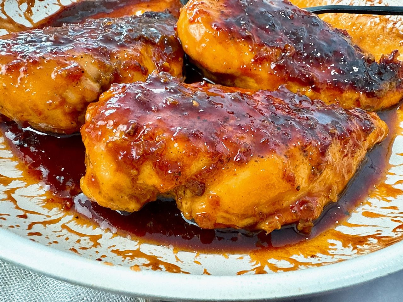 hot honey chicken in a white skillet with a black spoon