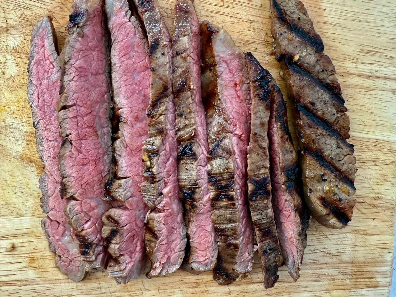 grilled flank steak slices on a wooden cutting board