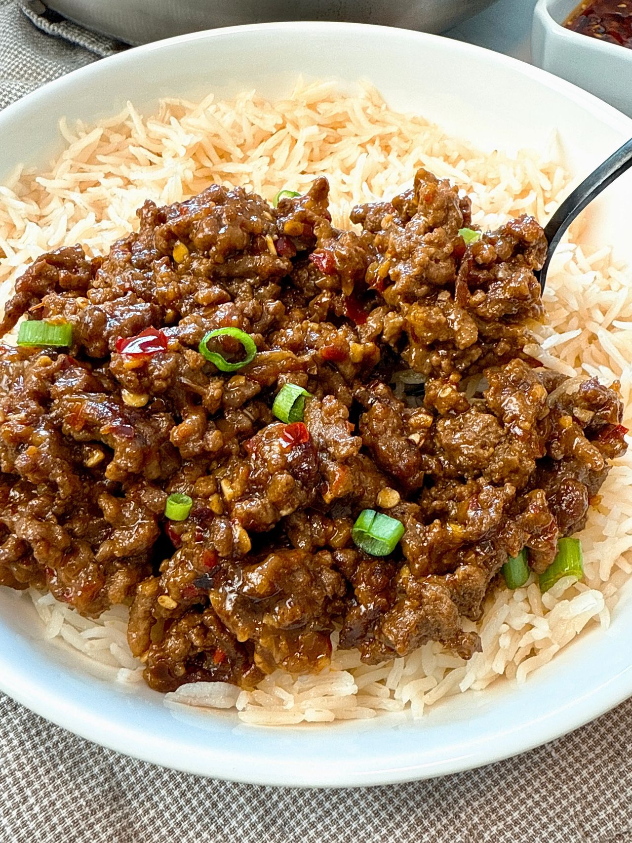Ground beef and chili crisp over rice in a white bowl