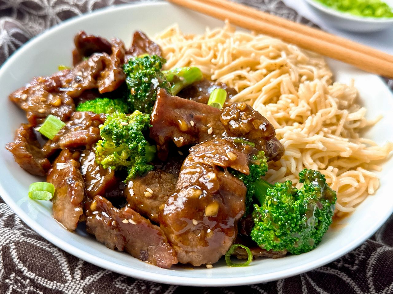 beef and broccoli on a white plate with Asian noodles