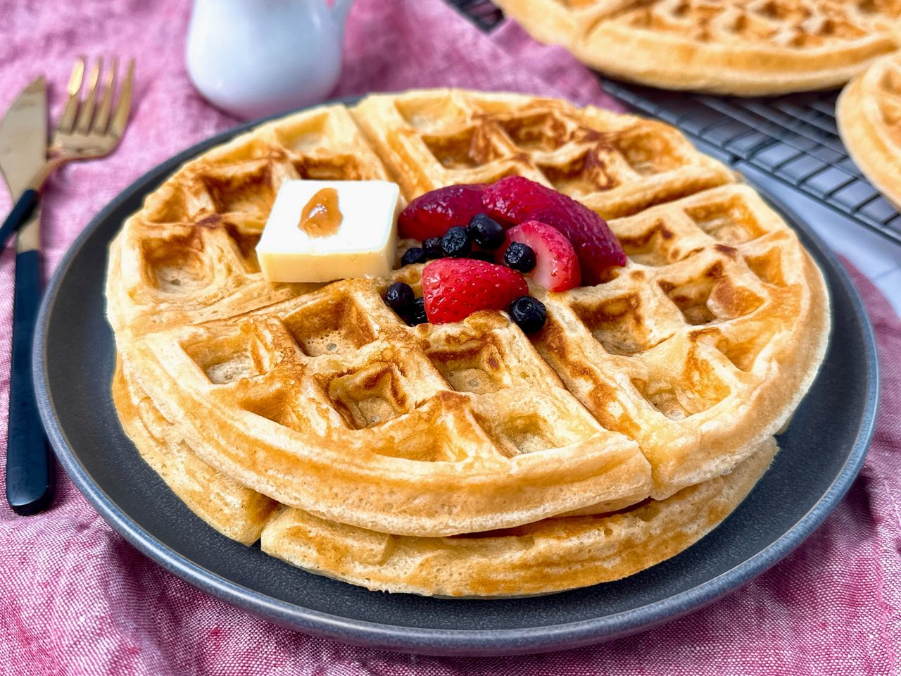 waffles on a grey plate with berries and butter