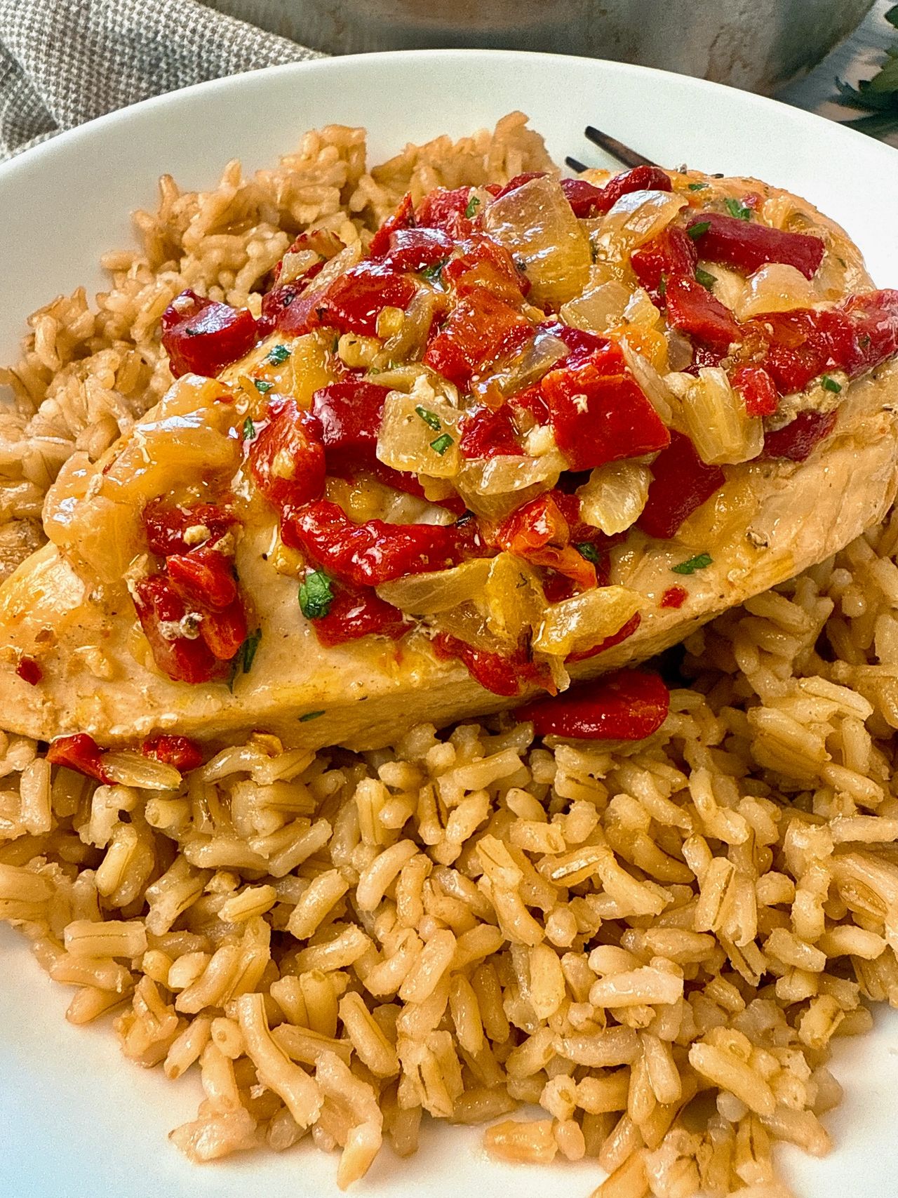 chicken breast with roasted red peppers over rice on a white plate