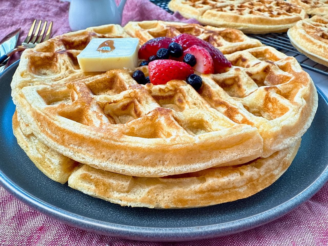 waffles on a grey plate with berries and butter