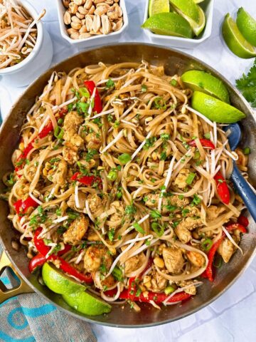 pad thai in a silver skillet with peanuts on the side